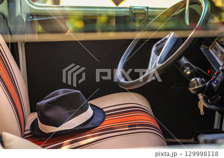 Salon with hat on seat. Interior of vintage car with striped seats and elegant fedora hat resting casually. Concept of retro lifestyle, stylish travel moments, adventure nostalgia Salon with hat on seat. Interior of vintage car with striped seats and elegant fedora hat resting casually. Concept of retro lifestyle, stylish travel moments, adventure nostalgia 129998118