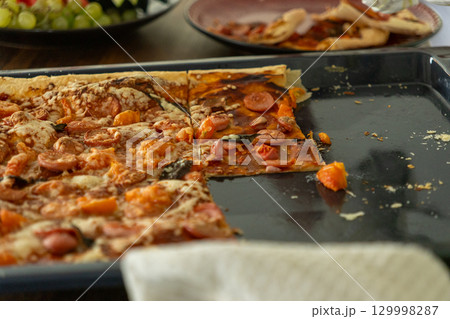 Pizza with pepperoni and sausages is cut in half and spread on a black frying pan. 129998287