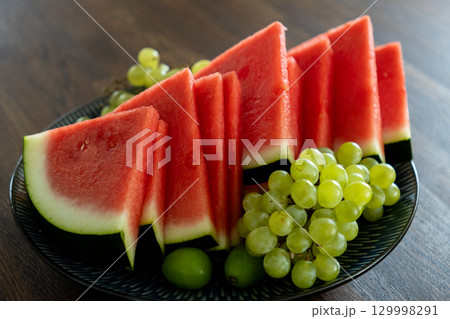plate with watermelon and grapes stands on wooden table. plate with watermelon and grapes stands on wooden table. 129998291