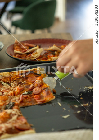 Pizza with pepperoni and sausages is cut in half and spread on a black frying pan. 129998293
