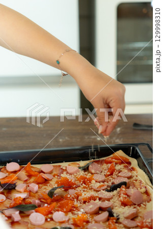 Making Pizza with pepperoni sausage cheese chef pours mozzarella on pizza in the kitchen. 129998310