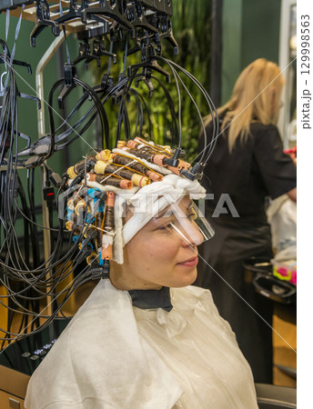 a young girl is getting her hair curled with curlers 129998563