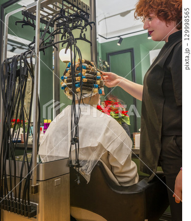 a young girl is getting her hair curled with curlers a young girl is getting her hair curled with curlers 129998565