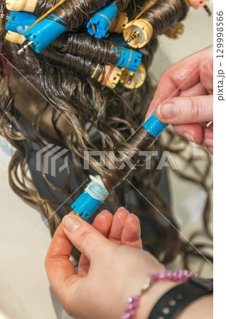 the hairdresser removes curlers from the client's hair. 129998566
