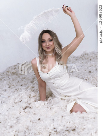 a very beautiful blonde sits in a white room in which feathers are flying a very beautiful blonde sits in a white room in which feathers are flying 129998622