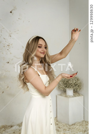 young beautiful blonde girl stands among feathers 129998630