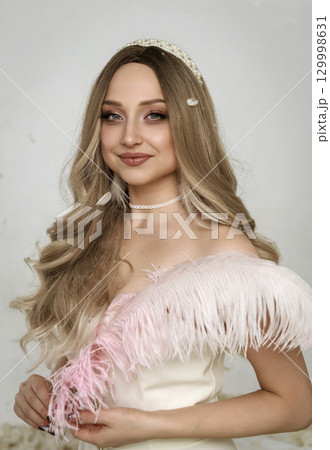 Portrait of a young blonde girl holding a pink feather 129998631
