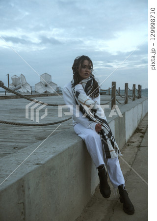 Beautiful young girl in a white tracksuit stands on the seashore in stormy weather 129998710