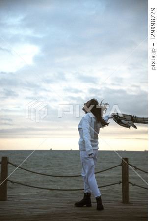 Beautiful young girl in a white tracksuit stands on the seashore in stormy weather Beautiful young girl in a white tracksuit stands on the seashore in stormy weather 129998729