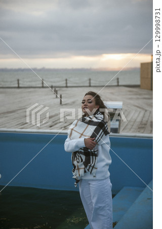Beautiful young girl in white tracksuit stands near big empty swimming pool Beautiful young girl in white tracksuit stands near big empty swimming pool 129998731