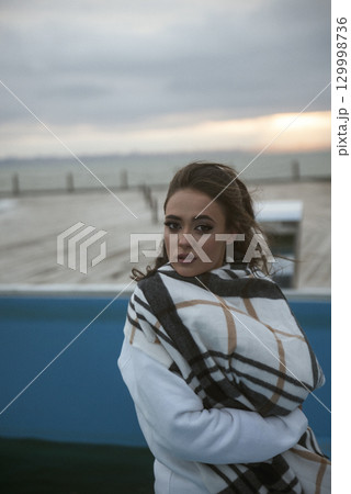 Beautiful young girl in a white tracksuit stands on the seashore in stormy weather 129998736