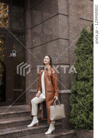 elegant woman over 40 exiting building with laptop bag elegant woman over 40 exiting building with laptop bag 129998802