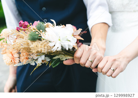 結婚指輪とブーケを持つ新郎新婦の手 129998927