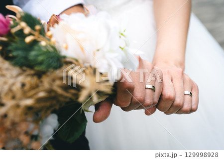 結婚指輪とブーケを持つ新郎新婦の手 結婚指輪とブーケを持つ新郎新婦の手 129998928