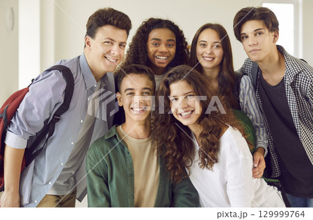 Group of a happy friends high school students standing together and looking cheerful at camera. 129999764