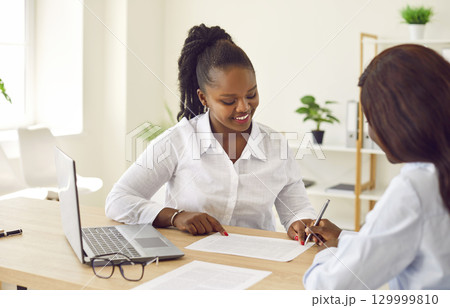 Two smiling business women working in office, reaching agreement or signing a contract. 129999810