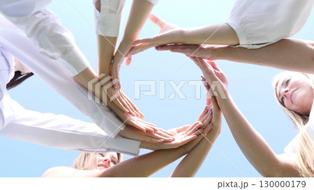 Various diverse hands have come together, united against a vivid, bright sky that represents unity and teamwork Various diverse hands have come together, united against a vivid, bright sky that represents unity and teamwork 130000179