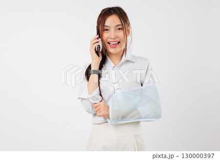 Smiling asian woman with broken arm talking phone in a sling after an accident, using her mobile phone and finding clinic address, recovery after injury with a phone, isolated studio white background Smiling asian woman with broken arm talking phone in a sling after an accident, using her mobile phone and finding clinic address, recovery after injury with a phone, isolated studio white background 130000397