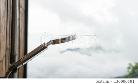 Stainless steel shower head. Attached to a wall panel made from bamboo sheets. Blurred image of the outside view of the sky clouds and shadows of trees. 130000591