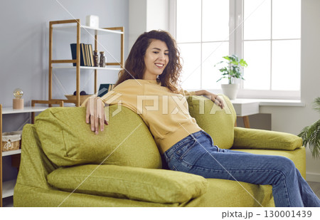 Happy young woman enjoying leisure time and relaxing on a comfortable green sofa at home 130001439