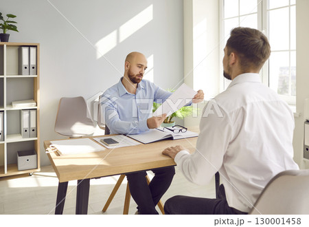 Man interviewing new candidate for vacancy company sitting in office holding and reading resume. 130001458