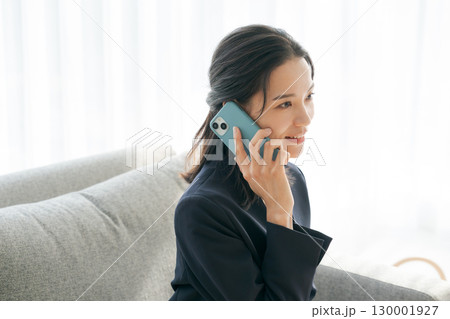 ソファーで電話をするスーツの女性 ソファーで電話をするスーツの女性 130001927