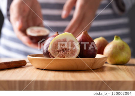 Fresh half fig and whole fruit on wooden plate and cutting wooden board with woman hand preparing 130002094
