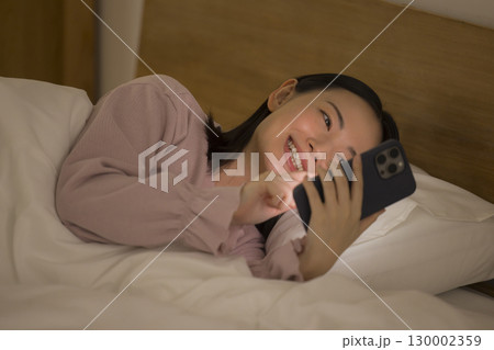ベッドでスマホを見る女性 130002359