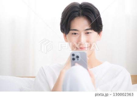 スマホを操作する若い男性　笑顔で見るクローズアップ 130002363