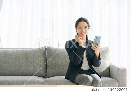 ソファーに座ってスマホを使う女性 ソファーに座ってスマホを使う女性 130002661