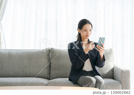ソファーに座ってスマホを使う女性 130002662