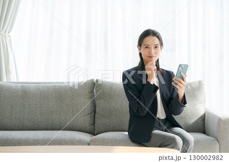 ソファーに座ってスマホを使う女性 130002982