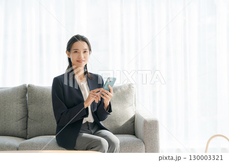 ソファーに座ってスマホを使う女性 ソファーに座ってスマホを使う女性 130003321