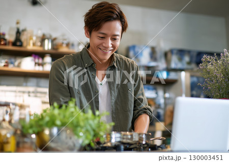 キッチンでパソコンを見ながら料理する笑顔の若い男性 キッチンでパソコンを見ながら料理する笑顔の若い男性 130003451