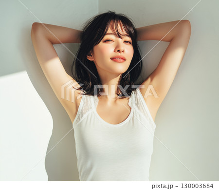 自然光を浴びて、腕を上げる白タンクトップ姿の20代日本人女性ポートレート（美容 ファッション 宣材） 130003684