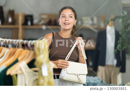 Girl customer choose handbag in store, and buyer carefully examines product. Girl customer choose handbag in store, and buyer carefully examines product. 130003881