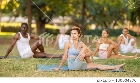 Woman performing Vakrasana during group yoga in summer park 130004270