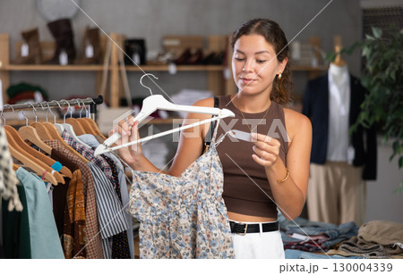 Girl customer choose crop top in store, and buyer carefully examines product. Girl customer choose crop top in store, and buyer carefully examines product. 130004339