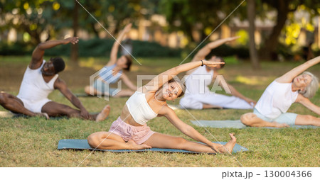 Girl stretching in Janu Sirsasana during group yoga in park 130004366