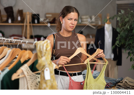 Distressed young woman customer in sales area of clothing store Distressed young woman customer in sales area of clothing store 130004411