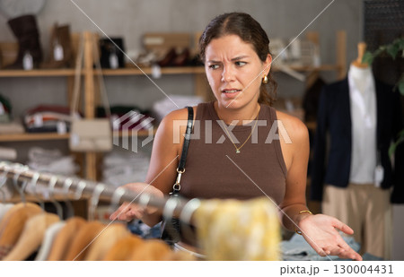 Young woman looking upset at clothes in store Young woman looking upset at clothes in store 130004431