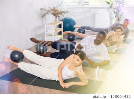 Group of active people doing soft ball pilates exercises during group pilates class in fitness gym 130004456