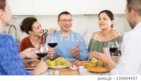 Middle-aged friends sitting at table with a glass of wine while having friendly conversation Middle-aged friends sitting at table with a glass of wine while having friendly conversation 130004457