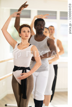 Graceful woman maintaining fourth position at ballet barre in studio 130004459