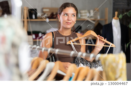 Girl customer choose crop top in store, and buyer carefully examines product. 130004467