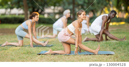 Girl doing Ardha Hanumanasana during group yoga in park Girl doing Ardha Hanumanasana during group yoga in park 130004528