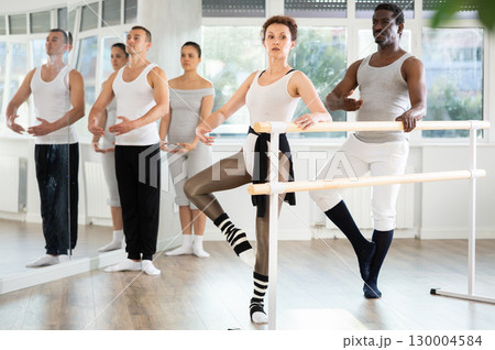 Woman and man dancers practice develope at barre 130004584