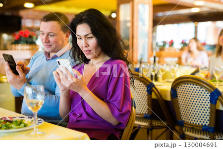 Man and woman look at the screen of his smartphones during lunch in restaurant 130004691