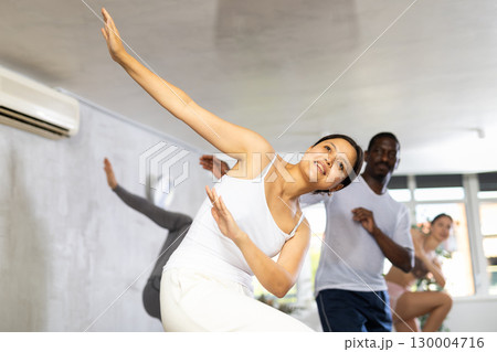 Group of happy sports woman and men in activewear exercising dynamic dancing movemens in gym studio 130004716