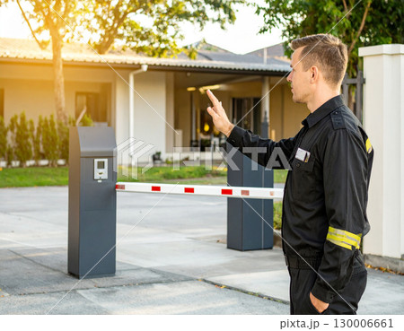 AI generated A professional security guard stands at the frame edge gesturing toward a guarded checkpoint with security booth barrier. The scene conveys safety, access control property protection. 130006661